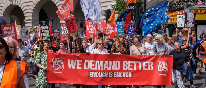 Union members marching behind a banner reading 'we demand better'