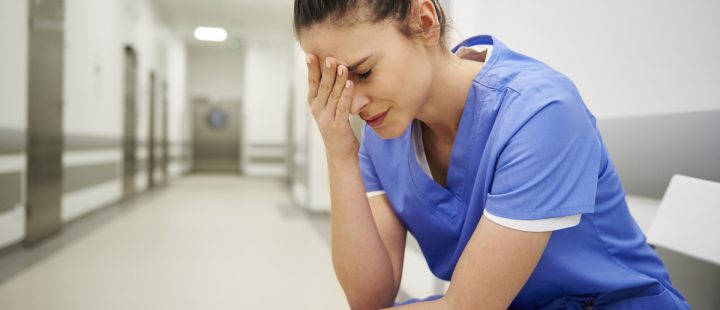 A nurse sitting in a hospital corridor with her hand to her head