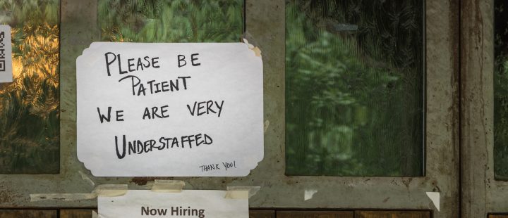 A handwritten sign in a window reading: 'Please be patient we are very understaffed'